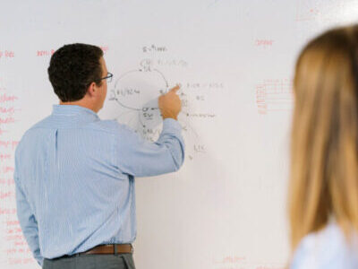 a man pointing at a white board referencing a graph