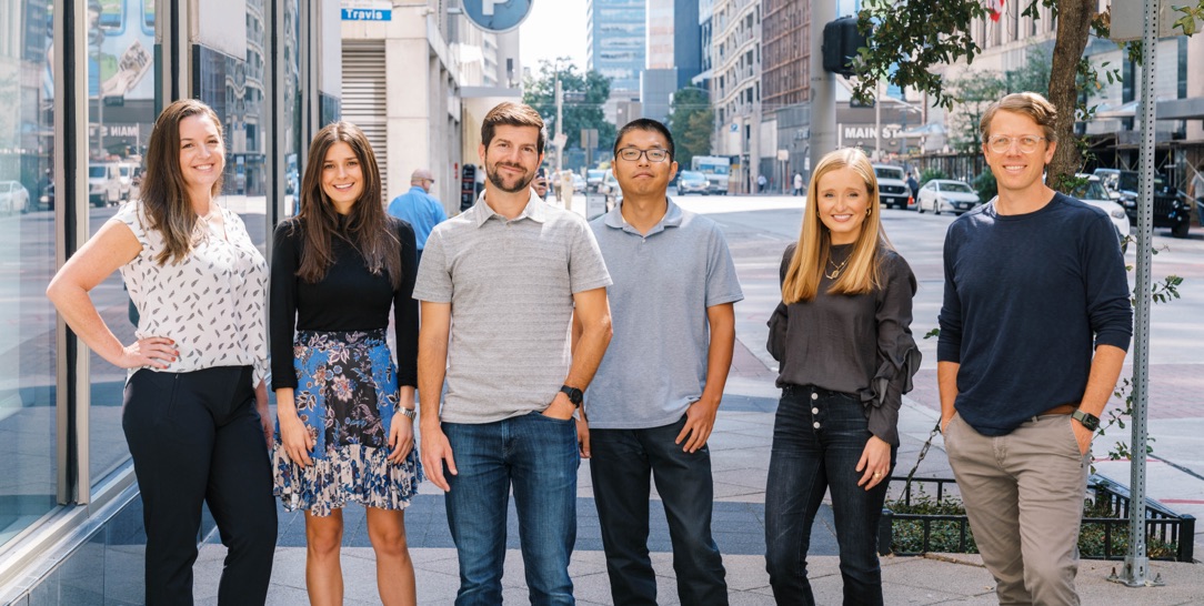 a group photo of 3 men and 3 women in business-casual clothing standing on the sidewalk in a city